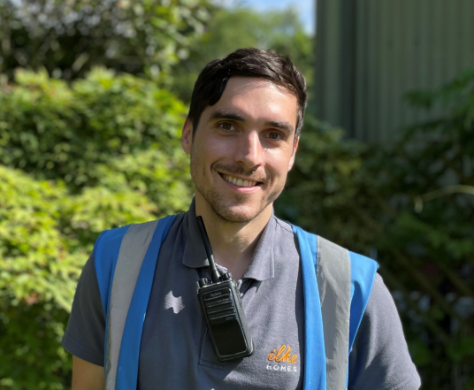 Person in a blue vest with a walkie-talkie standing outdoors.