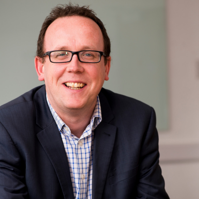 Person smiling in a suit with glasses, indoors