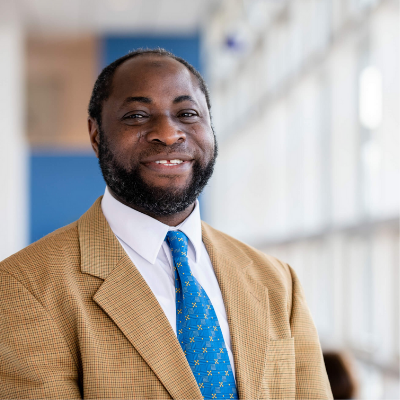 Person in a tan suit and blue tie smiling indoors.
