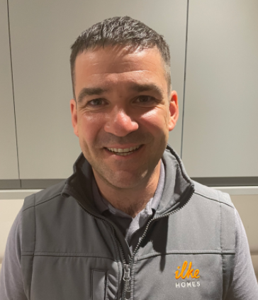 Person smiling and wearing a gray vest with 'ilke Homes' logo indoors.