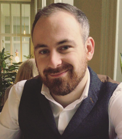 Person smiling indoors with plants in the background.