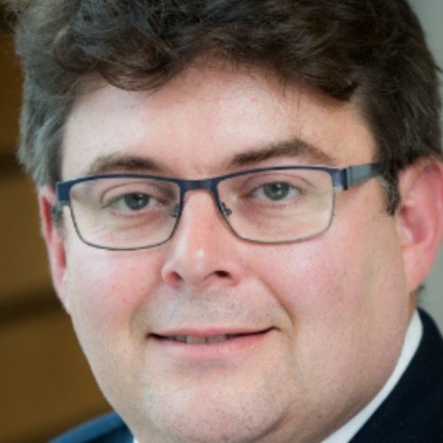 Person with glasses smiling softly at the camera.