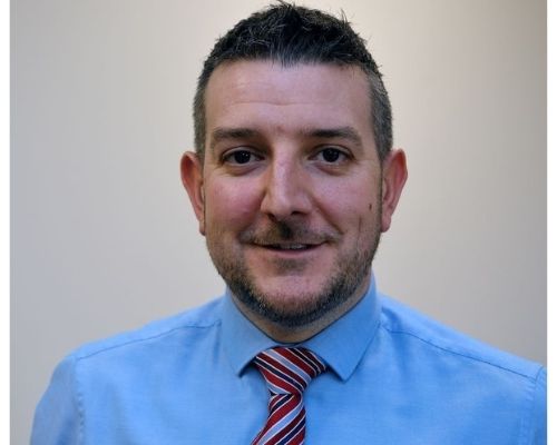A person smiling, wearing a blue shirt and red striped tie.