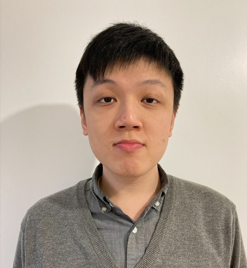 Person wearing a grey sweater and shirt, standing against a plain wall.