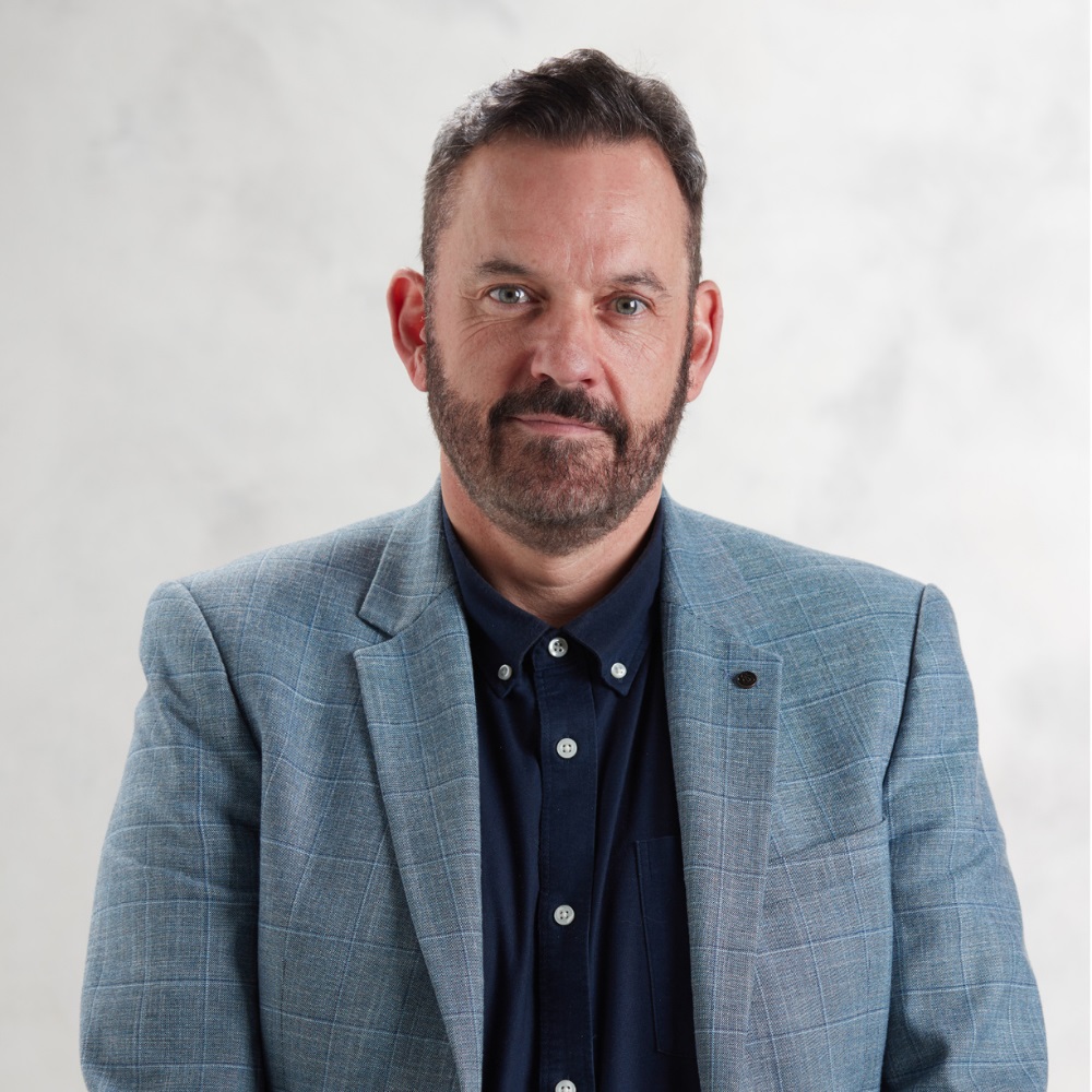 Person in blue blazer with a neutral expression.