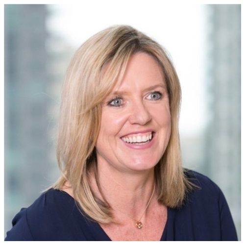 Person smiling in a professional setting with a blurred cityscape background.