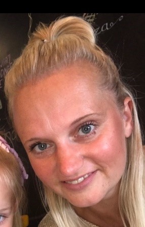 Smiling individual with light hair, sitting indoors, looking at the camera.