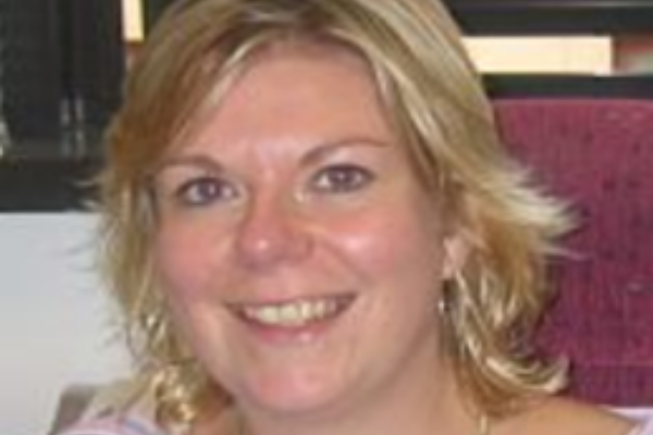 Person smiling with short hair indoors near a window.