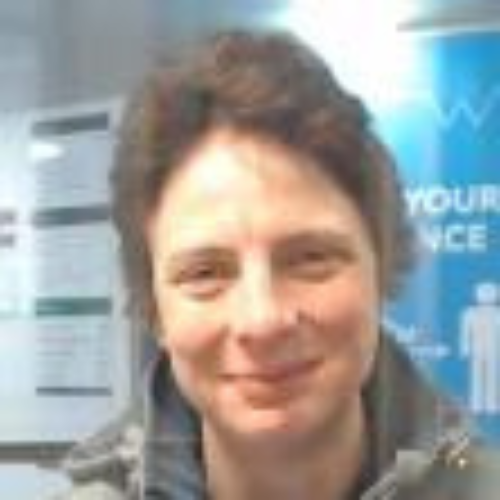 Person smiling inside a building, wearing a jacket.