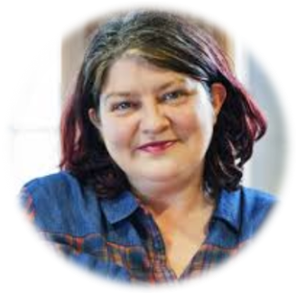 Person smiling warmly in a denim shirt indoors.