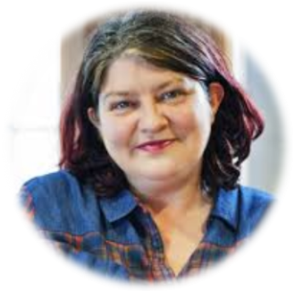 Person smiling warmly in a denim shirt indoors.