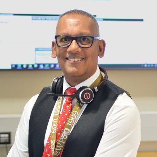 Person with glasses smiling, wearing a lanyard and headphones.