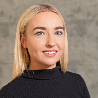 Person smiling in a black turtleneck sweater against a gray background.