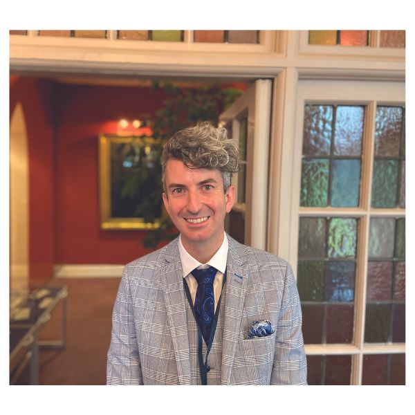 Person smiling in a suit with a patterned wall background.