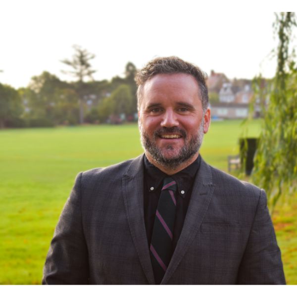 Person smiling in a suit with a grassy field in the background.