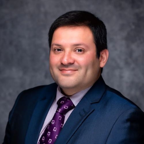 Person in a suit with a dark background.