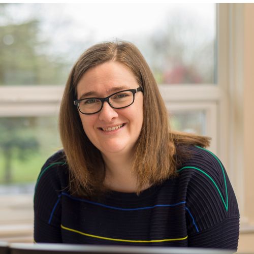 Person smiling indoors with a window view in the background.