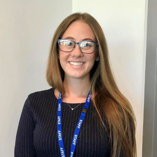A person wearing glasses, smiling and standing indoors with a staff lanyard.