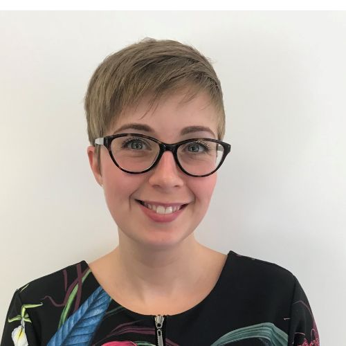 Person smiling with short hair and glasses against a white background.