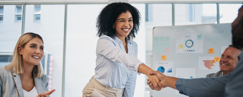 top uk cities for finance recruitment A woman engages in a handshake with two individuals in an office, representing a professional meeting or agreement