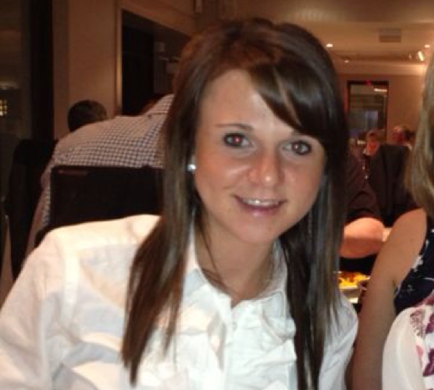 Person smiling at a restaurant, sitting at a table with others in the background.