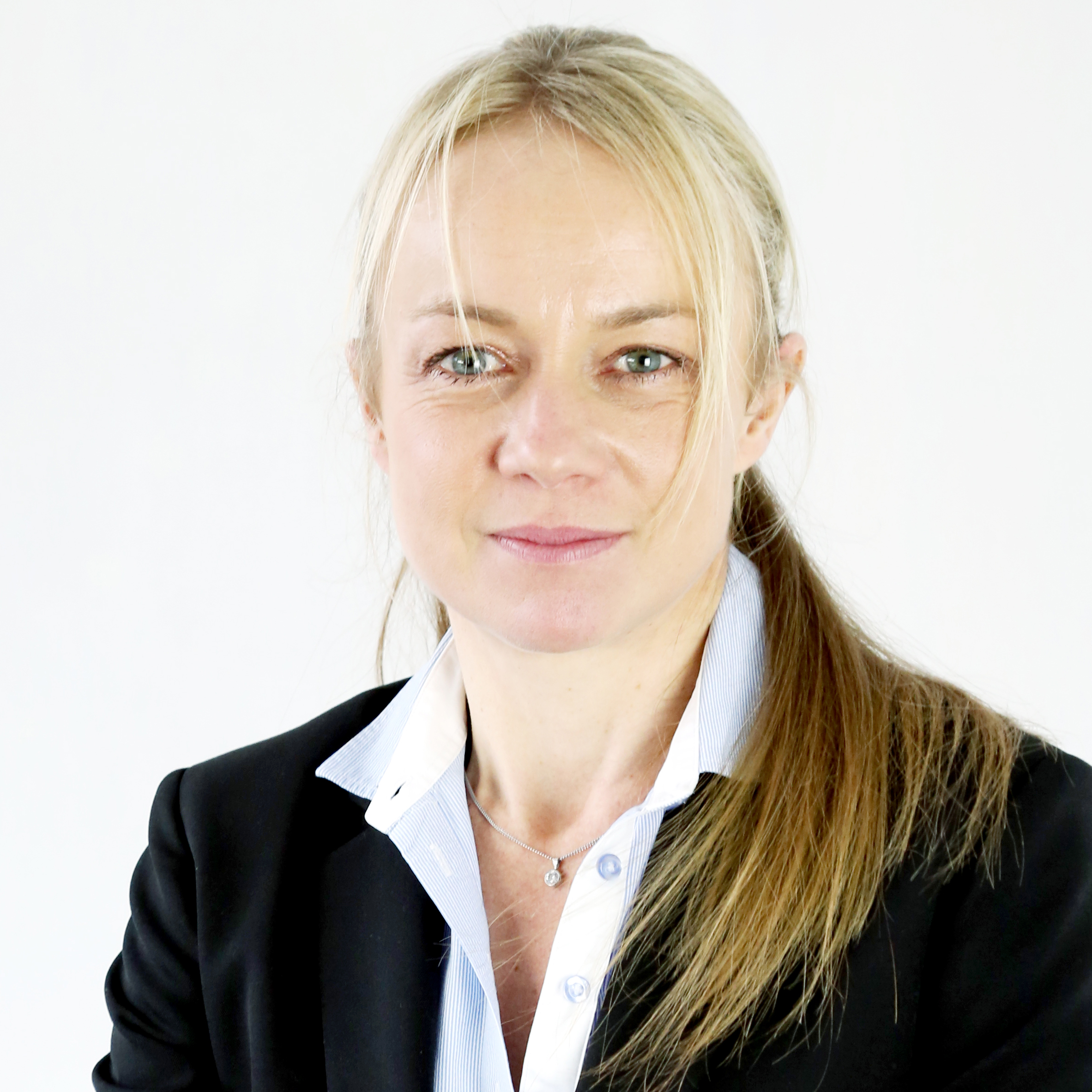 Person in a black blazer with light hair tied back, smiling softly.