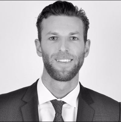 Portrait of a smiling person in a suit and tie against a plain background.