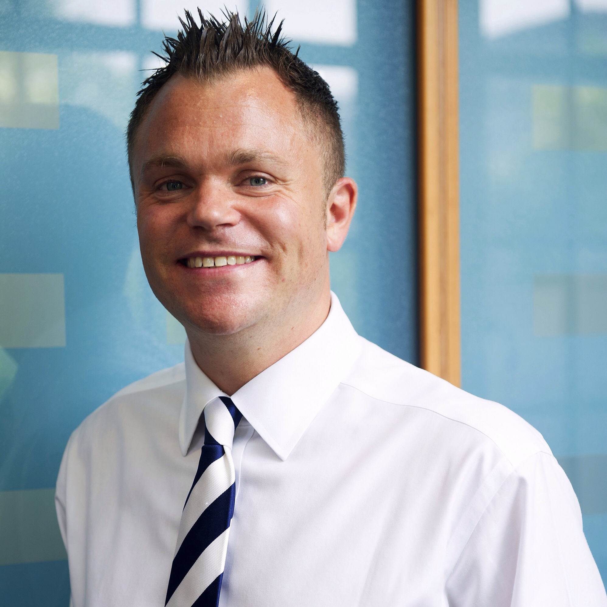 Person smiling in business attire with a striped tie, standing in front of a blue background.
