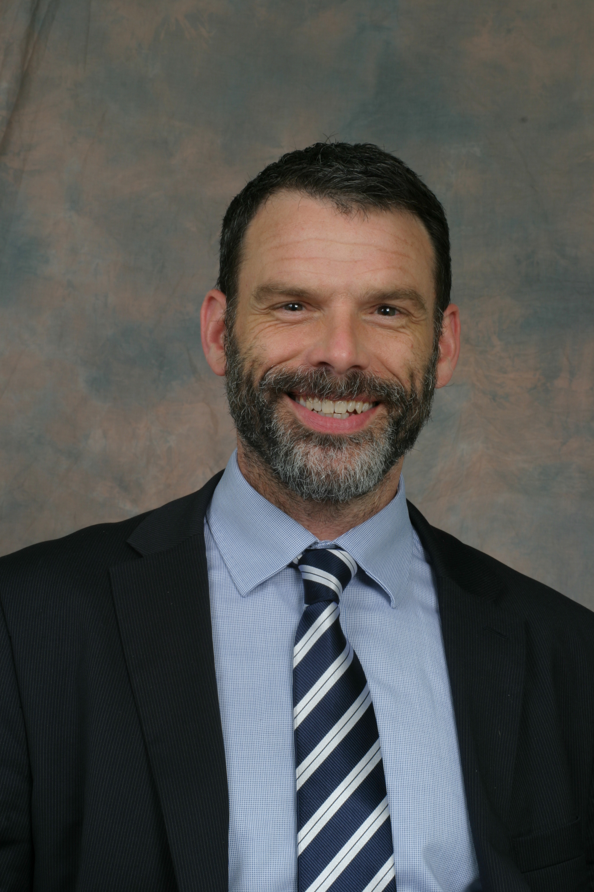 Person in a suit smiling in front of a neutral backdrop.