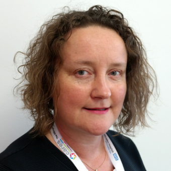 Person with curly hair wearing a lanyard, smiling lightly.
