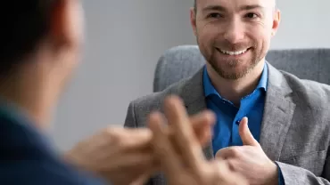 Smiling person with a beard giving a thumbs-up during a conversation.
