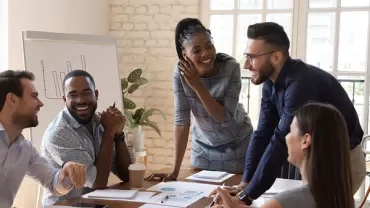 Group of people smiling around a conference table during a meeting.