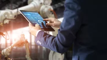 Person using a tablet to control robotic machinery in a factory.
