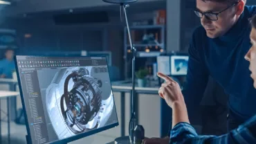 Two people discussing a 3D model on a computer screen in an office.