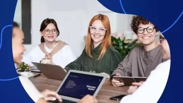 Group of people smiling at a conference table with laptops.