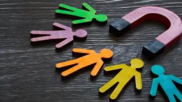 Colorful figures attracted to a magnet on wooden background.