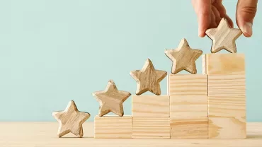 Hand placing wooden star on blocks arranged in steps.