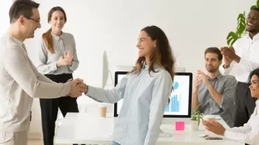 Colleagues applauding as two people shake hands in an office.