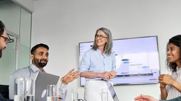 Group of people in a meeting room discussing with a presentation screen in the background.