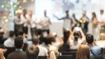 A group of people attending a conference, with many using smartphones.