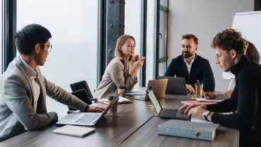 People in a meeting room discussing ideas with laptops and a whiteboard.