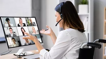 Person on video call, wearing headset, gesturing towards screen with multiple participants displayed.