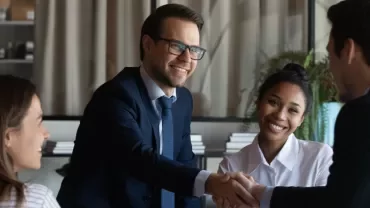 Colleagues smiling and shaking hands during a meeting.