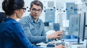 Two colleagues discussing work at a computer in an office.