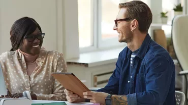 Two colleagues smiling and discussing work in a bright office.