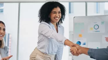 A woman engages in a handshake with two individuals in an office, representing a professional meeting or agreement