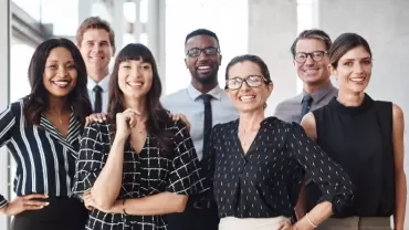 Diverse group of professionally dressed adults smiling in a office setting.