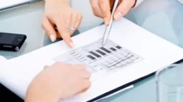 Two people discussing a document with bar graphs at a table.