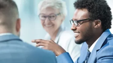 Three people engaged in a business meeting, one person speaking.