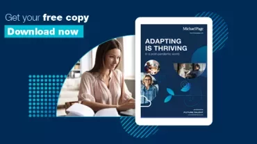 Person working at a desk with a book titled 'Adapting is Thriving'.